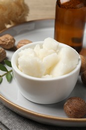 Photo of Shea butter in bowl and nuts on table, closeup