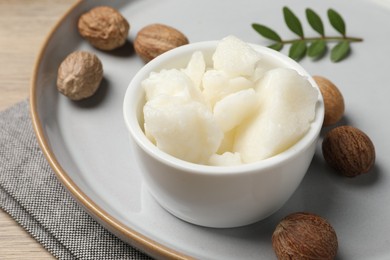 Photo of Shea butter in bowl and nuts on wooden table, closeup