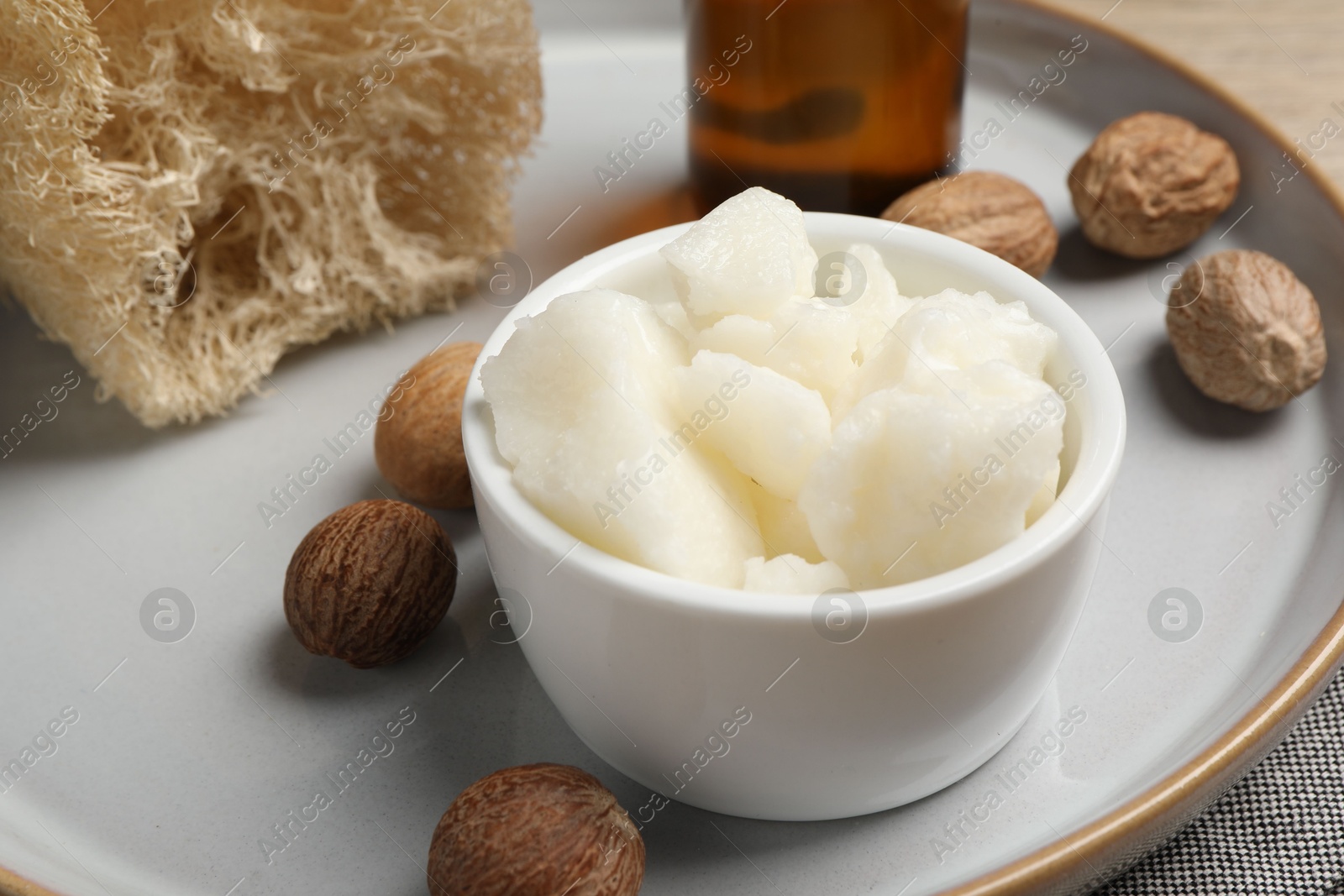 Photo of Shea butter in bowl and nuts on table, closeup