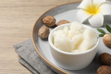 Photo of Shea butter in bowl, flower and nuts on wooden table, closeup