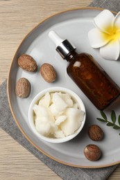 Photo of Shea butter, bottle, flower and nuts on wooden table, top view