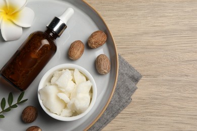 Photo of Shea butter, bottle, flower and nuts on wooden table, top view. Space for text