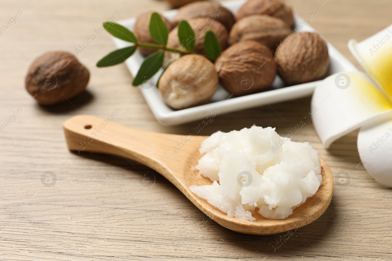 Photo of Shea butter in spoon, flower and nuts on wooden table, closeup