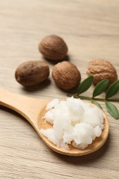 Photo of Shea butter in spoon and nuts on wooden table, closeup