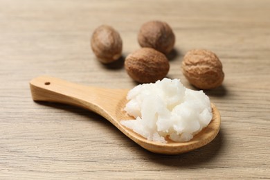 Shea butter in spoon and nuts on wooden table, closeup