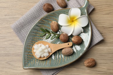 Photo of Shea butter in spoon, flower and nuts on wooden table, top view