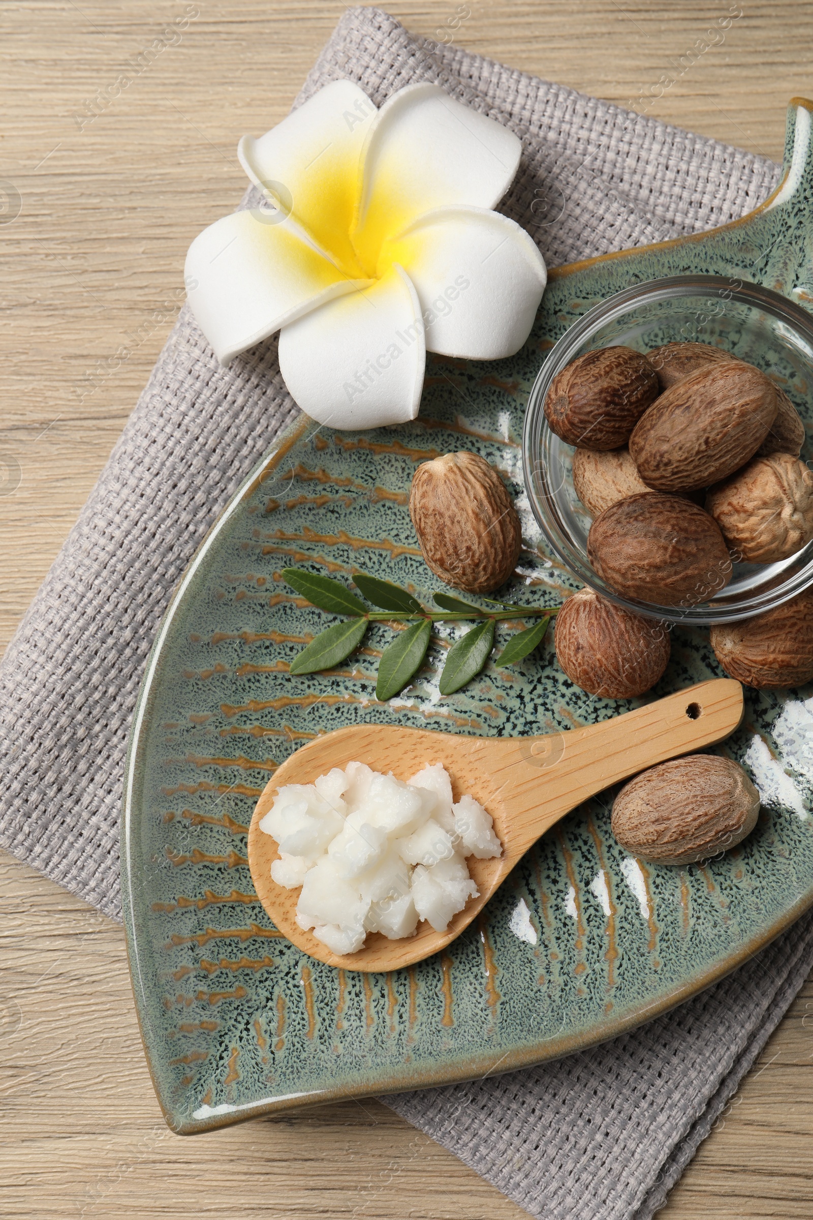 Photo of Shea butter in spoon, flower and nuts on wooden table, top view