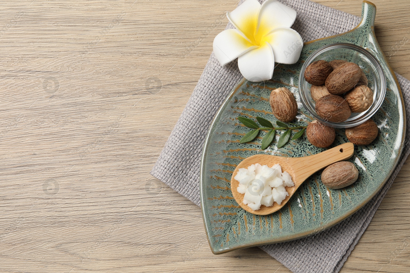 Photo of Shea butter in spoon, flower and nuts on wooden table, top view. Space for text