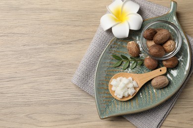 Shea butter in spoon, flower and nuts on wooden table, top view. Space for text