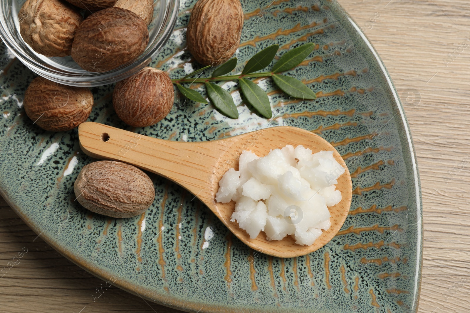 Photo of Shea butter in spoon and nuts on wooden table, top view