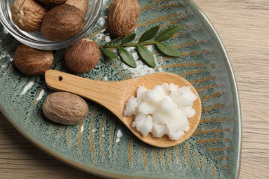 Shea butter in spoon and nuts on wooden table, top view