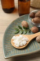 Shea butter in spoon and nuts on wooden table, closeup