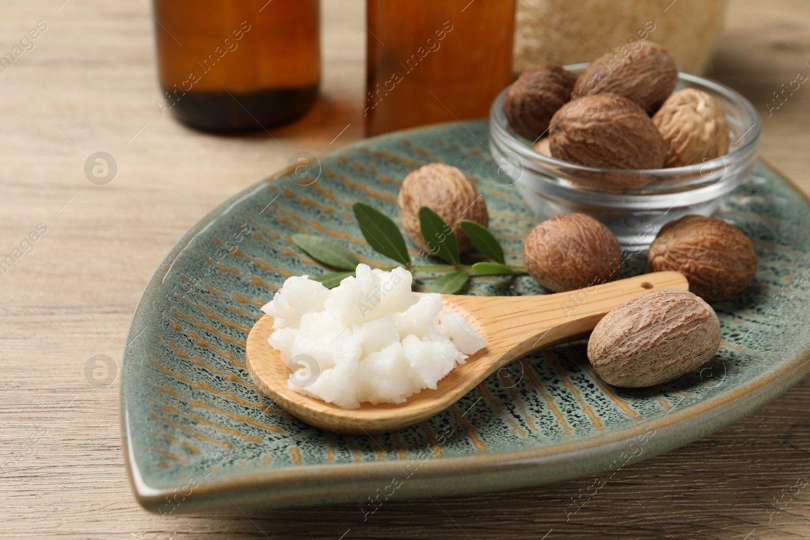 Photo of Shea butter in spoon and nuts on wooden table, closeup