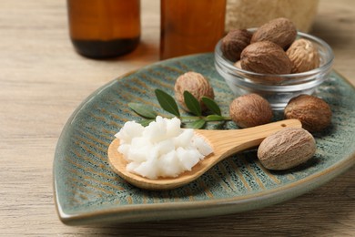 Shea butter in spoon and nuts on wooden table, closeup