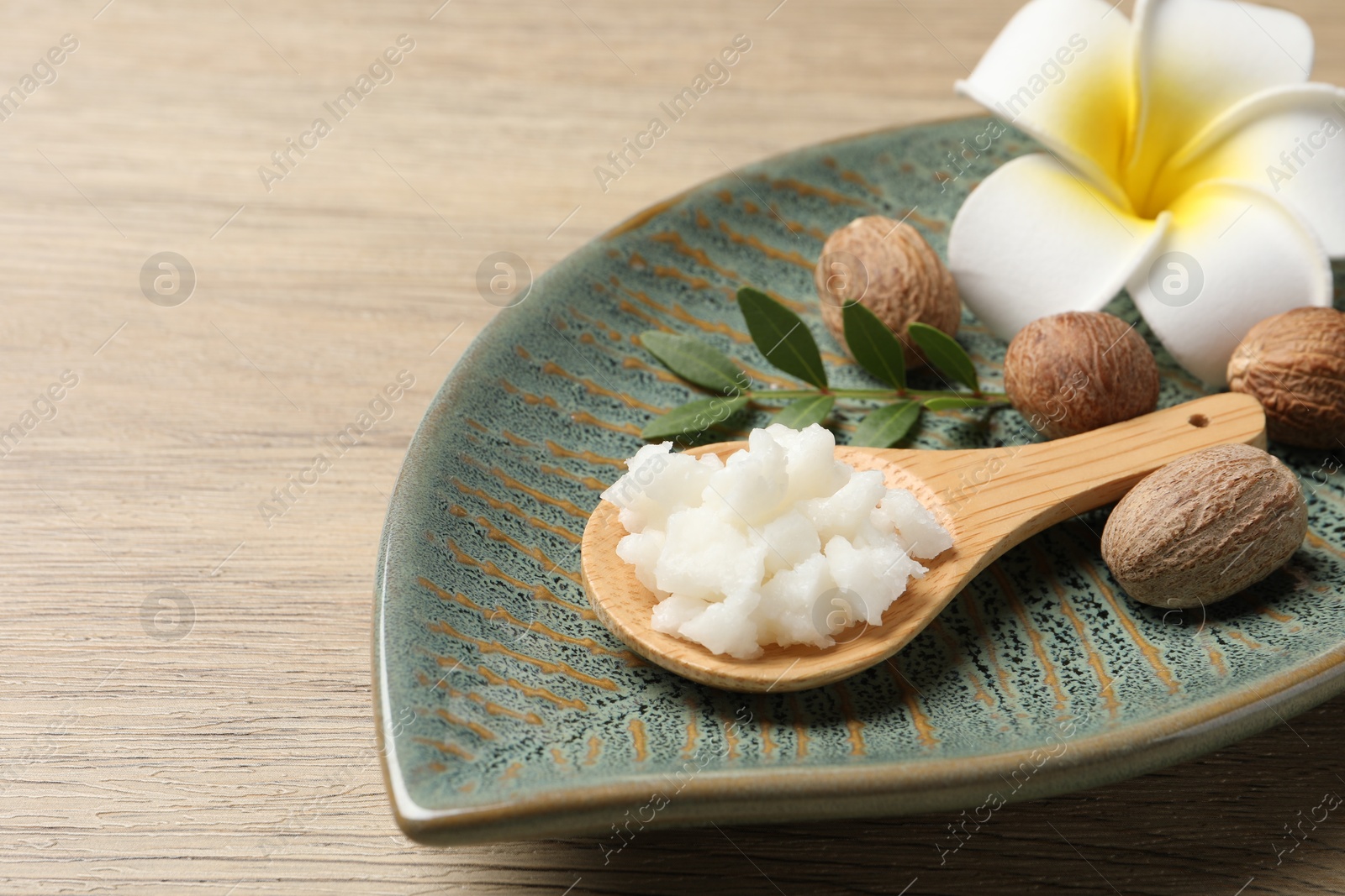 Photo of Shea butter in spoon, flower and nuts on wooden table, closeup. Space for text