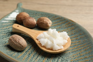 Shea butter in spoon and nuts on wooden table, closeup