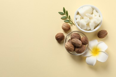 Photo of Shea butter in bowl, flower and nuts on beige background, flat lay. Space for text