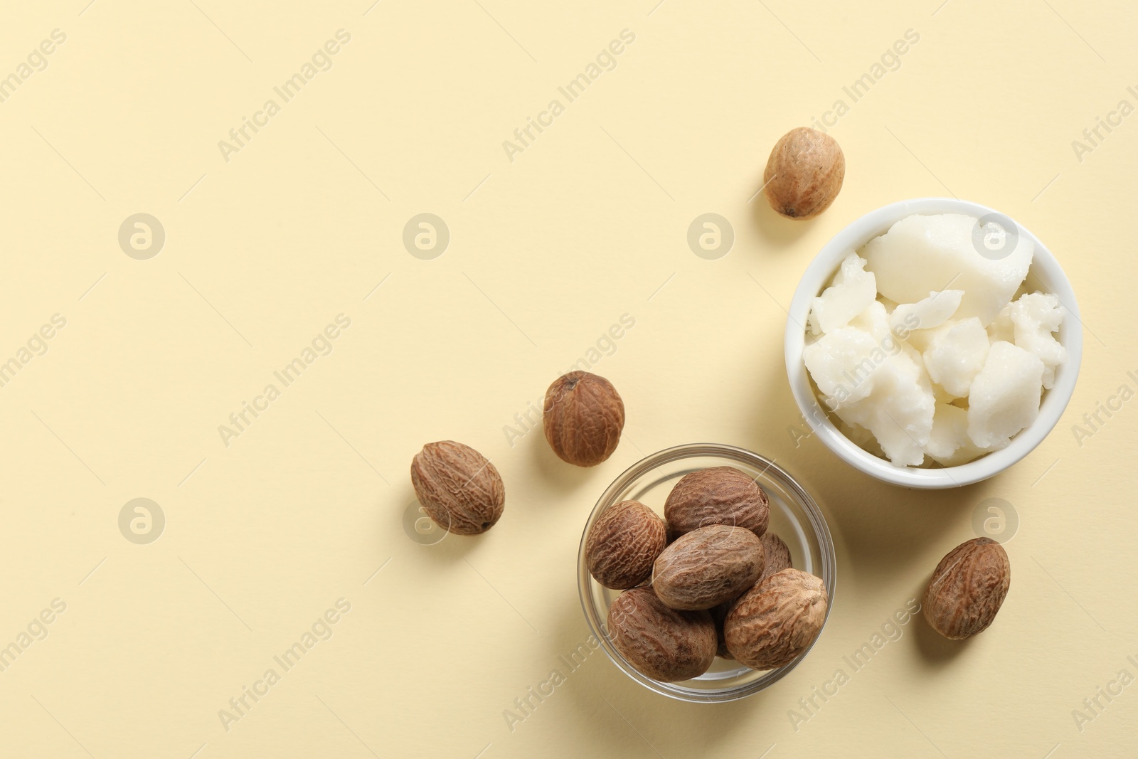 Photo of Shea butter in bowl and nuts on beige background, flat lay. Space for text