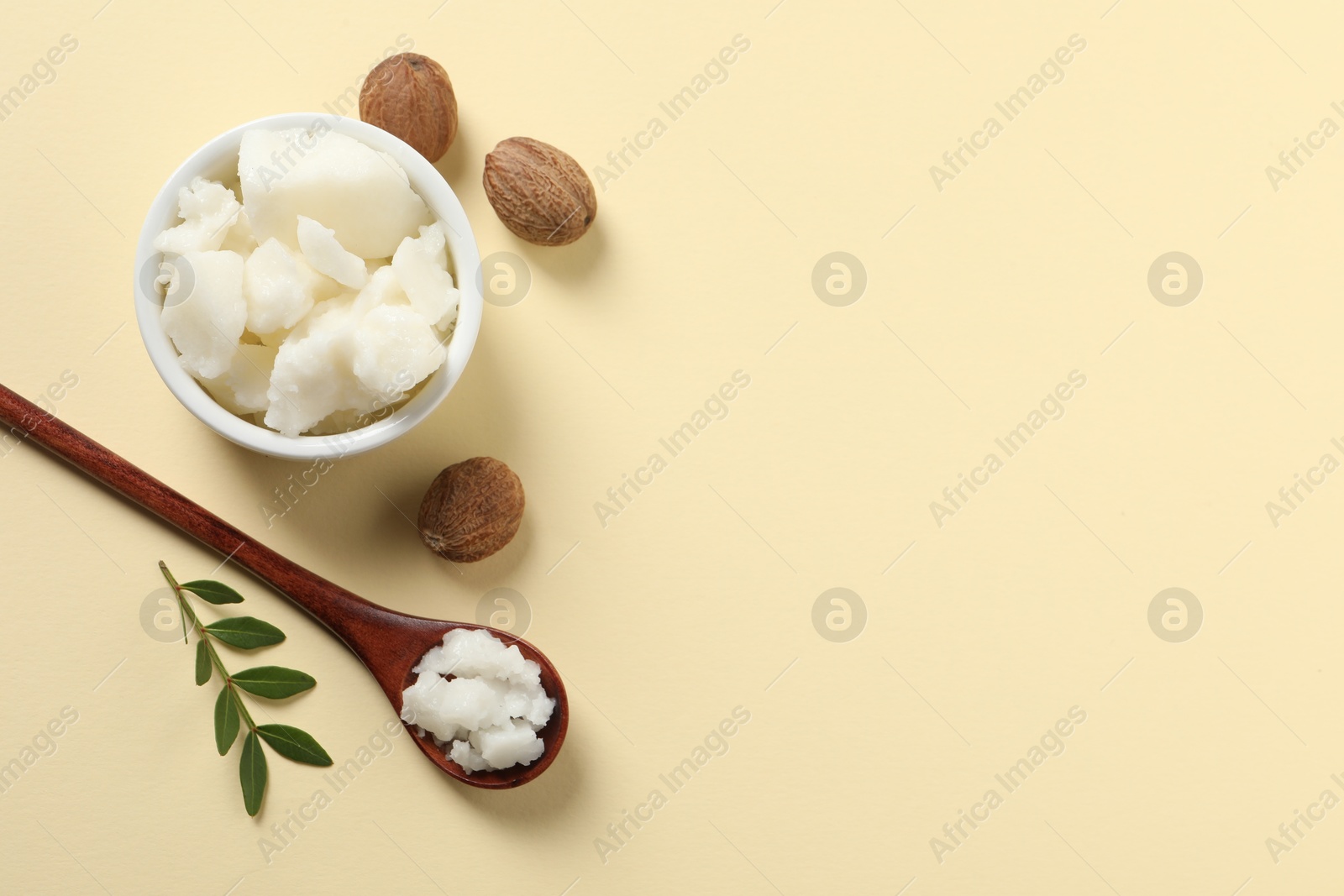 Photo of Shea butter in bowl, spoon and nuts on beige background, flat lay. Space for text