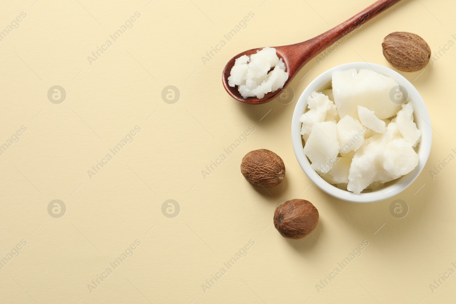 Photo of Shea butter in bowl, spoon and nuts on beige background, flat lay. Space for text