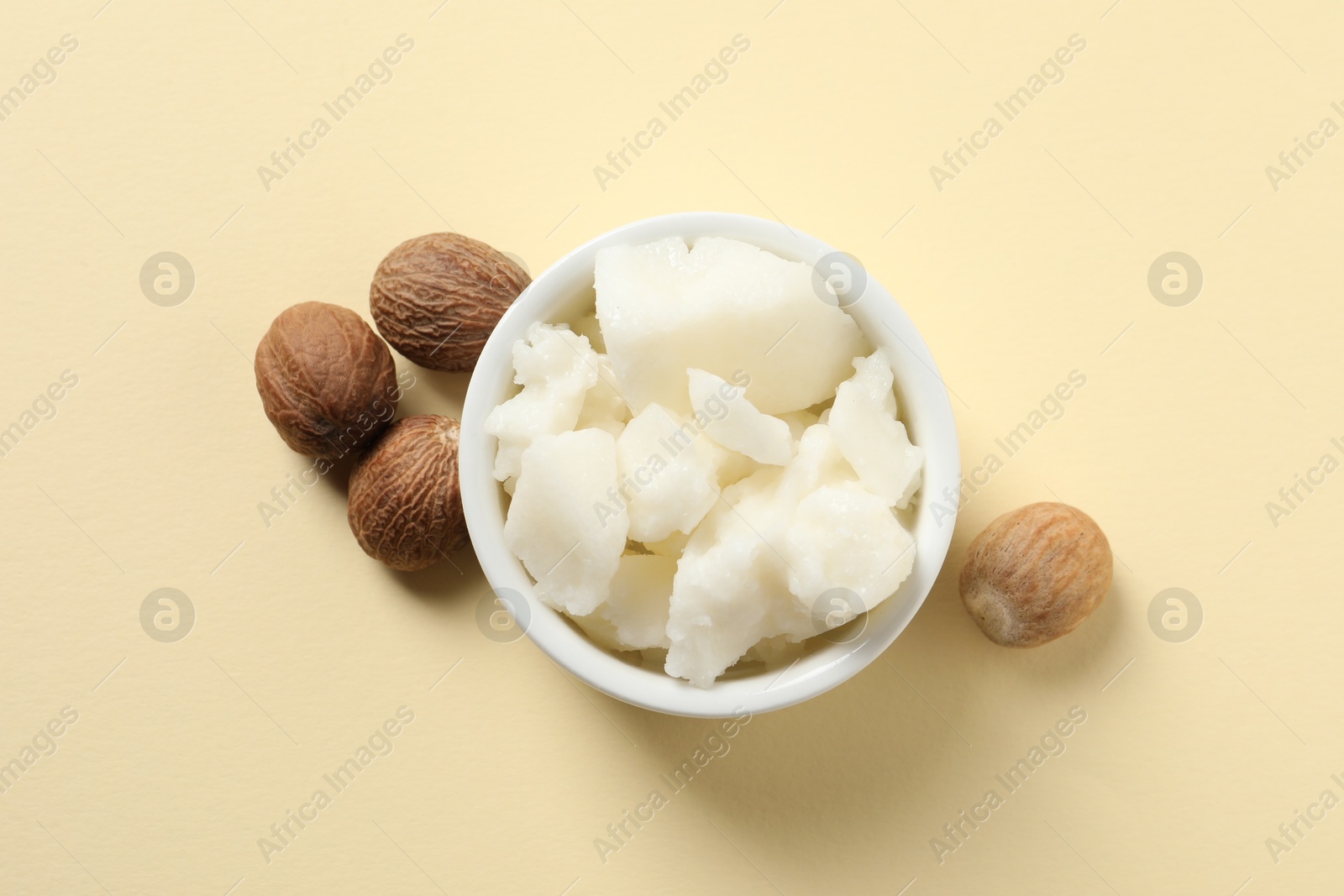 Photo of Shea butter in bowl and nuts on beige background, top view