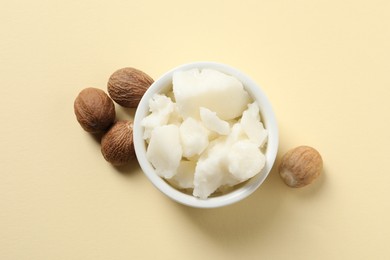 Shea butter in bowl and nuts on beige background, top view