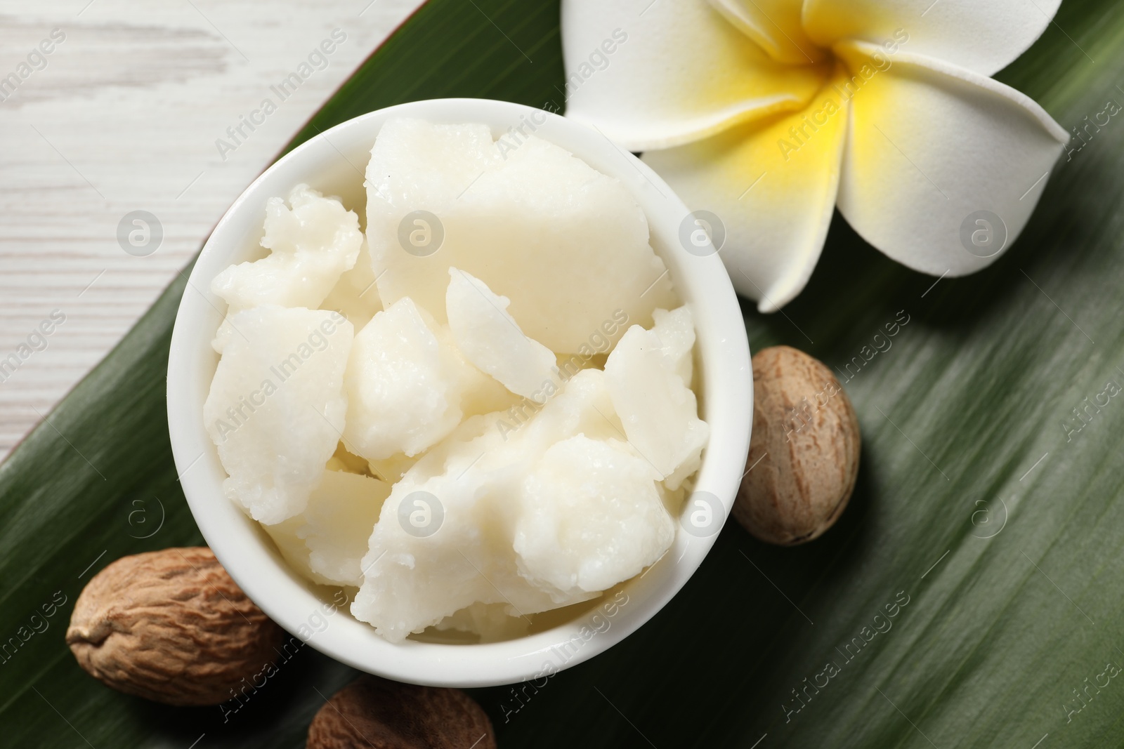 Photo of Shea butter in bowl, flower and nuts on white wooden table, flat lay