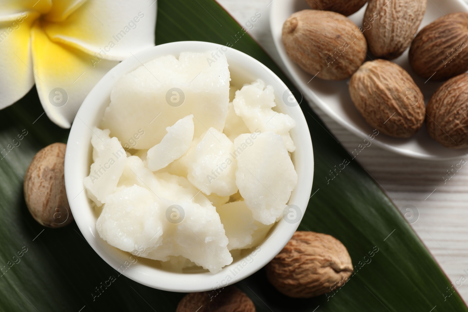 Photo of Shea butter in bowl, flower and nuts on white wooden table, flat lay