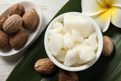 Shea butter in bowl, flower and nuts on white wooden table, flat lay