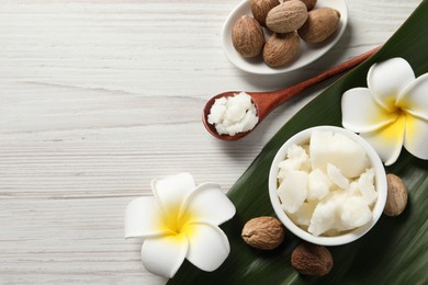 Photo of Shea butter in bowl, spoon, flowers and nuts on white wooden table, flat lay. Space for text