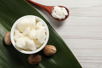 Shea butter in bowl, spoon and nuts on white wooden table, flat lay. Space for text