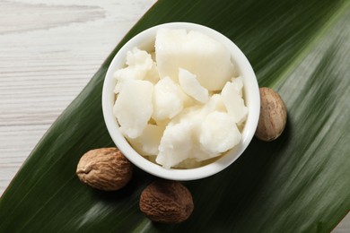 Shea butter in bowl and nuts on white wooden table, flat lay