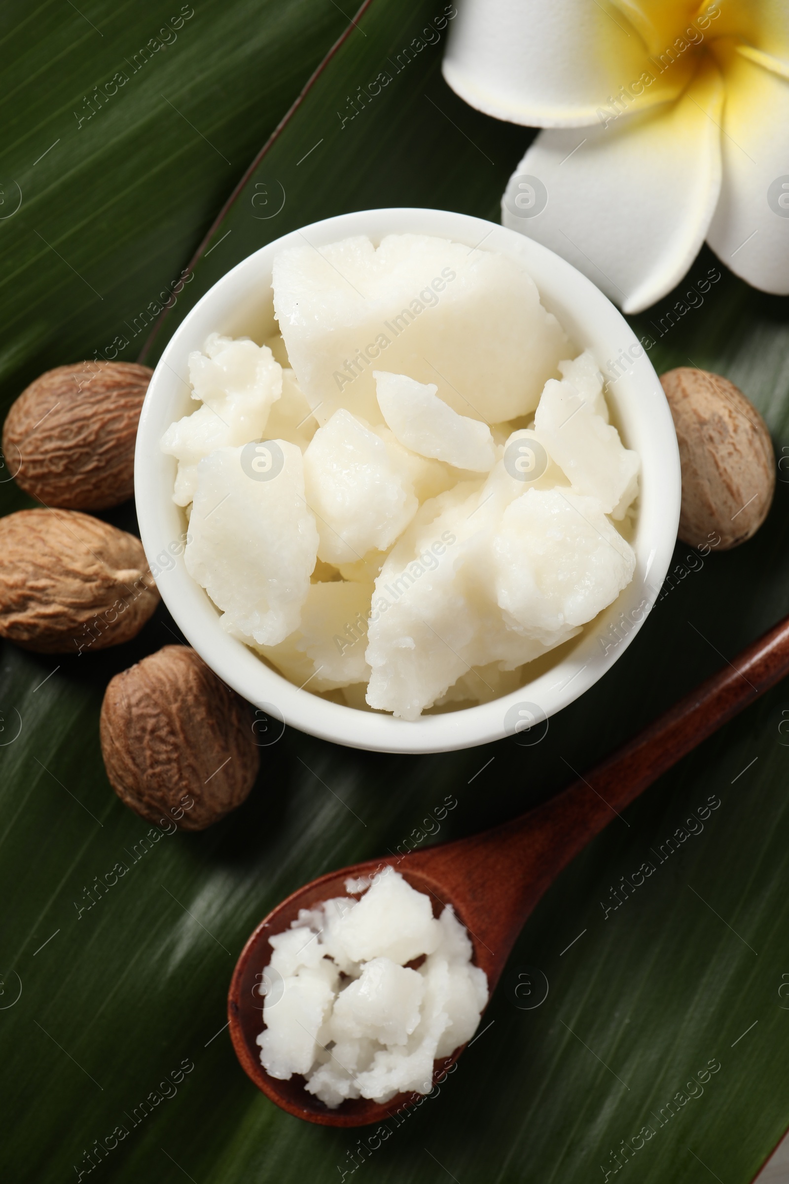 Photo of Shea butter in bowl, spoon, flower and nuts on table, flat lay