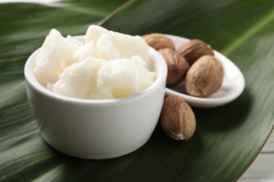 Photo of Shea butter in bowl and nuts on white wooden table, closeup