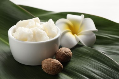 Shea butter in bowl, flower and nuts on table, closeup