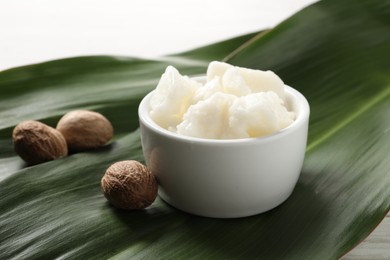 Shea butter in bowl and nuts on white wooden table, closeup