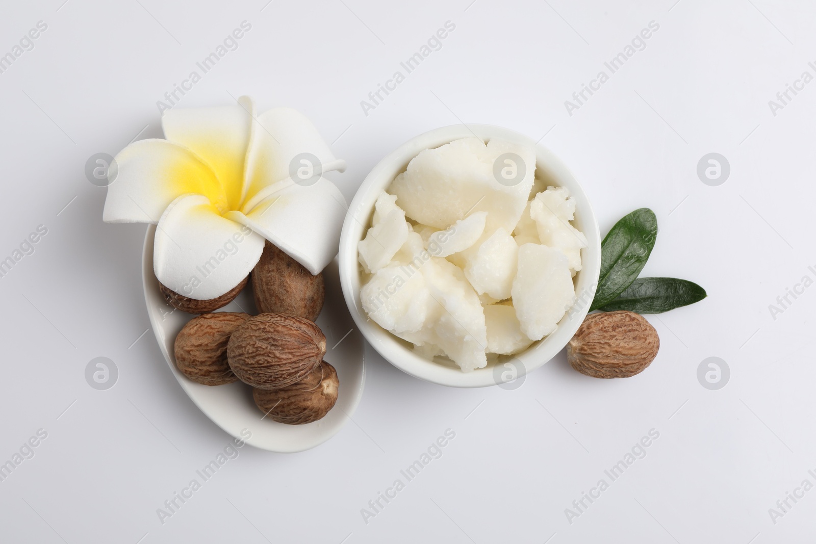 Photo of Shea butter in bowl, flower and nuts on white background, flat lay