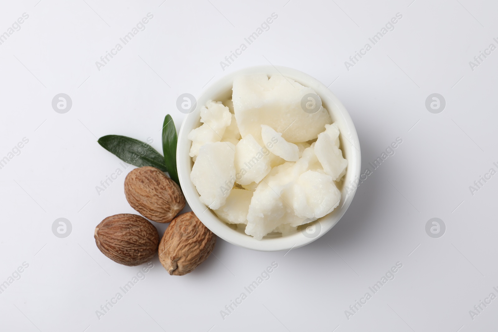 Photo of Shea butter in bowl and nuts on white background, flat lay