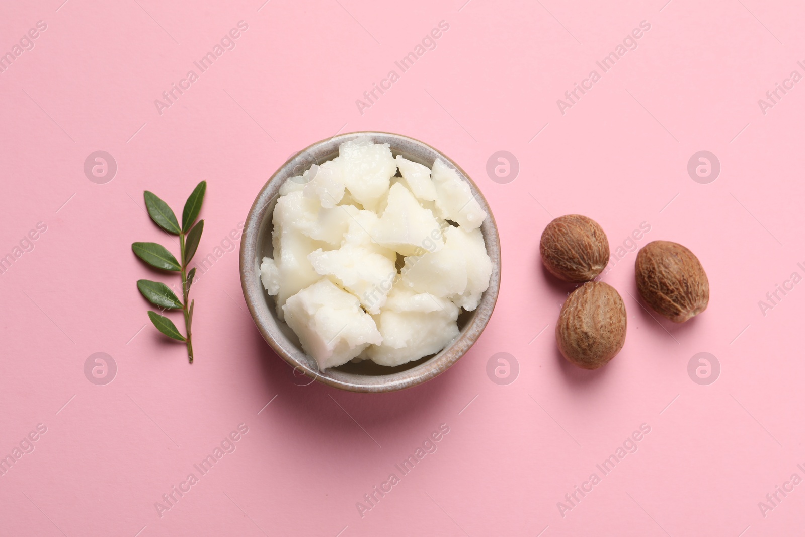 Photo of Shea butter in bowl and nuts on pink background, flat lay