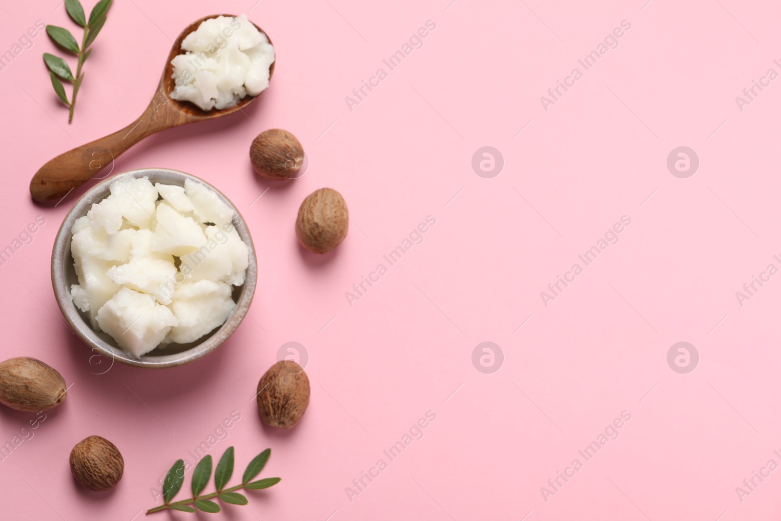 Photo of Shea butter in bowl, spoon and nuts on pink background, flat lay. Space for text