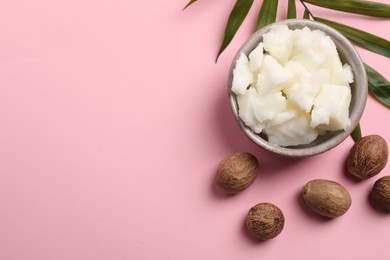 Photo of Shea butter in bowl and nuts on pink background, flat lay. Space for text