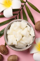 Photo of Shea butter in bowl, flowers and nuts on pink background, flat lay