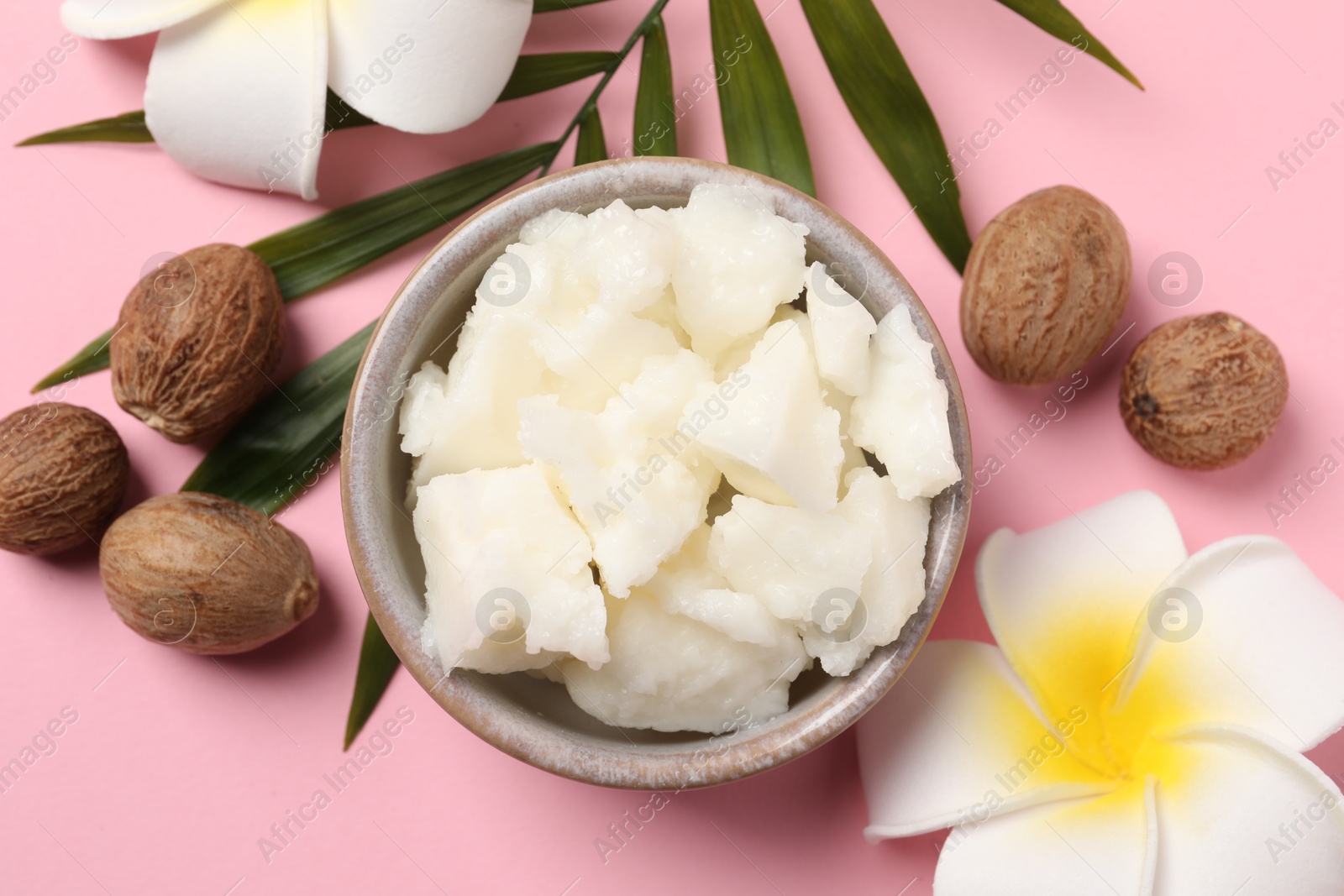 Photo of Shea butter in bowl, flowers and nuts on pink background, flat lay