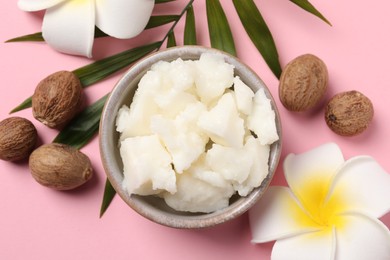 Shea butter in bowl, flowers and nuts on pink background, flat lay