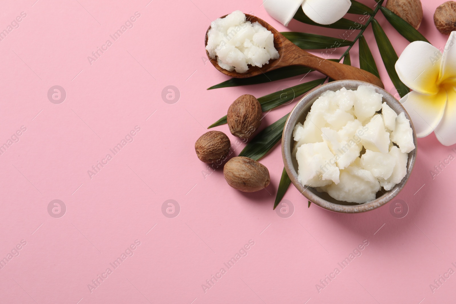 Photo of Shea butter in bowl, flower and nuts on pink background, flat lay. Space for text