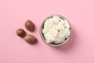 Shea butter in bowl and nuts on pink background, flat lay