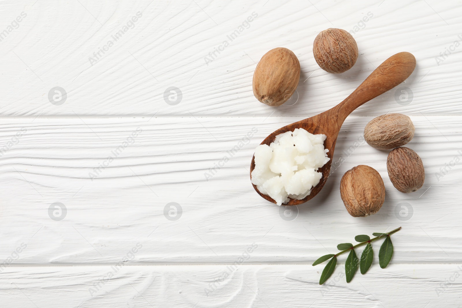 Photo of Shea butter in spoon and nuts on white wooden table, top view. Space for text