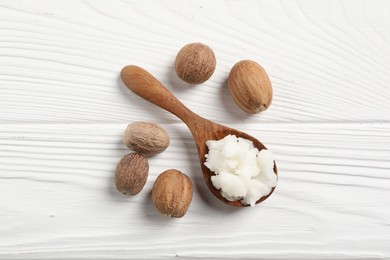 Shea butter in spoon and nuts on white wooden table, top view