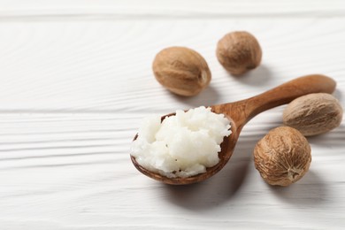 Shea butter in spoon and nuts on white wooden table, closeup. Space for text