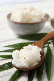 Shea butter in spoon and nuts on white wooden table, closeup